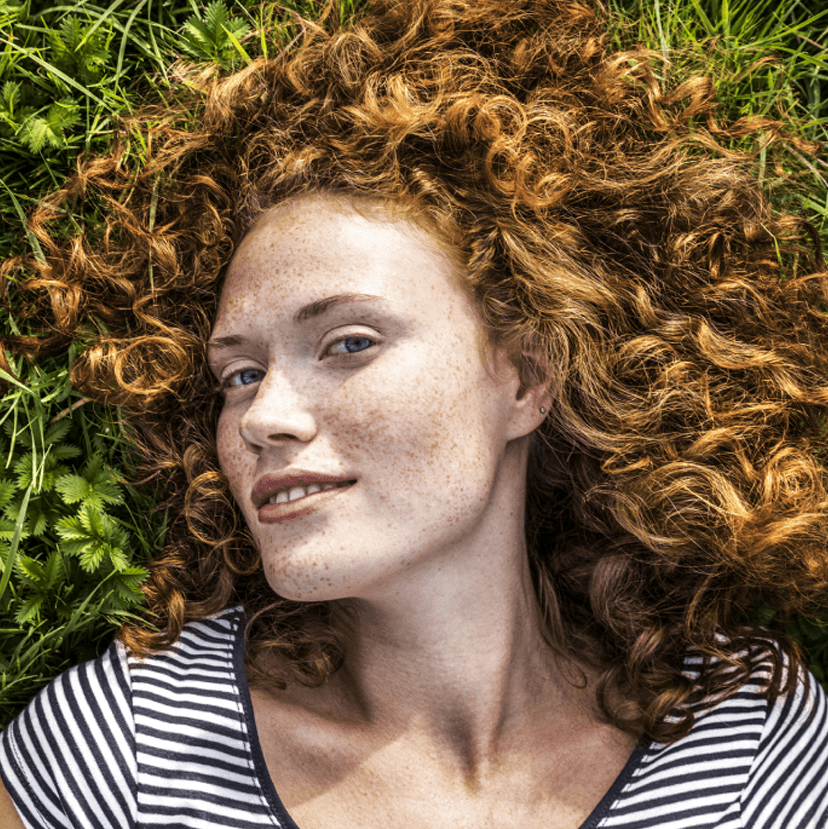 A woman lies on grass in the sun, smiling